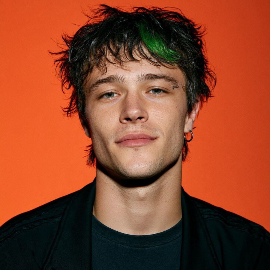 Portrait of Jean Claude, a young man with dark tousled hair, a green streak and a hoop earring against an orange background